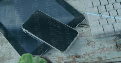 Smartphone resting on tablet with keyboard and code overlay on weathered wood workspace