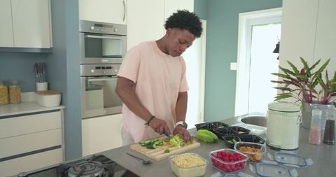 Young man preparing meal-prep salads on kitchen island with containers and fresh produce