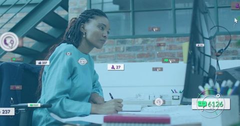 African american woman monitoring analytics while writing notes in modern loft workspace