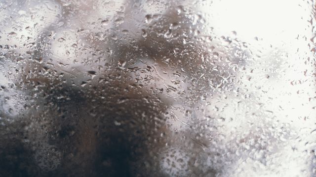 Detailed close-up view of raindrops on window glass with an abstract blurred background. Suitable for weather-related content, website backgrounds, or illustrating themes of melancholy and calm. Can be used as a background for rain music playlists, weather forecasts, or inspirational quotes.
