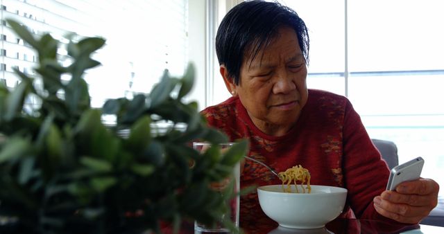 Senior Woman Enjoying Noodles at Home While Using Smartphone - Download Free Stock Images Pikwizard.com