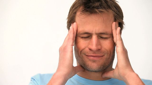 A mid-aged caucasian man is holding his head with closed eyes, indicating a headache or stress. This video could be used in health articles, stress management tips, pharmaceutical adverts, or wellness blogs. The light background highlights the man's expression of discomfort.