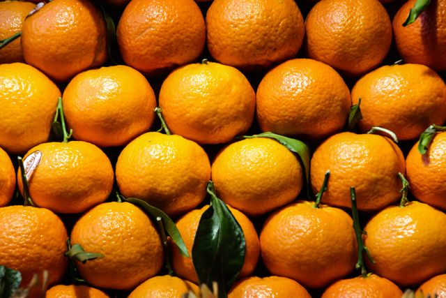 Bright oranges with green leaves stacked closely together, showcasing their fresh, juicy appeal. Suitable for use in health and nutrition articles, grocery store advertisements, fresh produce promotional materials, or as a background for healthy food blogs.