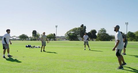 Five men practicing team drills on sunny grass field outdoor teamwork training session