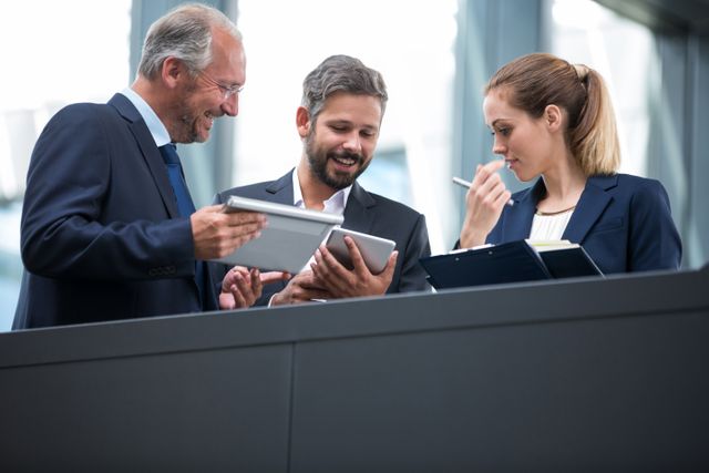 Business professionals are discussing over a digital tablet in a modern office environment. This image can be used to depict teamwork, collaboration, and corporate meetings. It is ideal for business presentations, corporate websites, and articles about business strategy and communication.