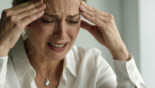 Mature woman pressing temples wincing from headache and anxiety in bright minimal interior
