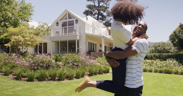 Happy diverse couple embracing and laughing outside house in sunny garden, copy space. Summer, home, romance, relationship, togetherness, domestic life and lifestyle, unaltered.