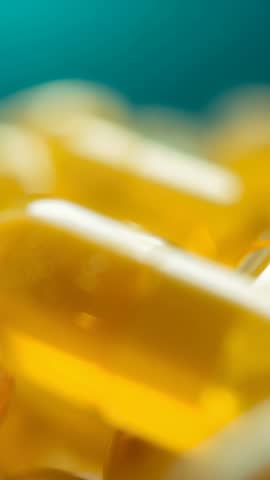 Vertical macro video shifting focus revealing amber softgels and bubbles on teal backdrop