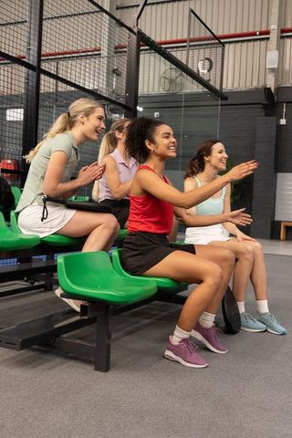 Diverse women cheering at indoor padel court, clapping from green bleachers