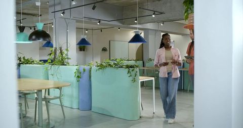 African american coworkers walking and speaking in pastel coworking space with greenery