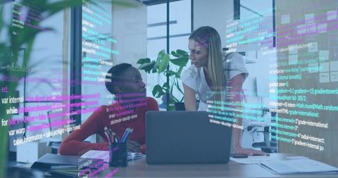 Women collaborating over laptop with transparent code overlay in modern office workspace