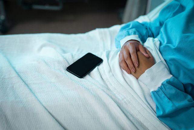 Biracial female patient lying on hospital bed with smartphone. medical and healthcare services at hospital.