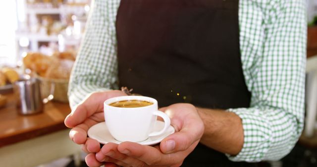 Barista holding a cup of fresh coffee in a cozy cafe, perfect for illustrating scenes of professional service and hospitality in a coffee shop or restaurant. Great for marketing materials, advertisements, and articles focused on coffee culture.
