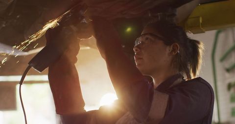 Female mechanic grinding metal in dim workshop