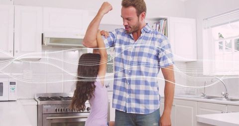 Playful father-daughter moment in bright kitchen with dad lifting arm and child reaching