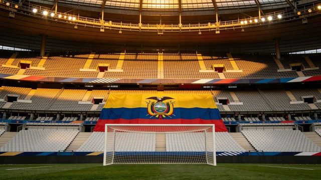 Ecuador flag draped over stadium seats behind soccer goal under warm golden evening lights