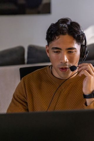 Young man wearing headset adjusting microphone while working remotely from home on laptop