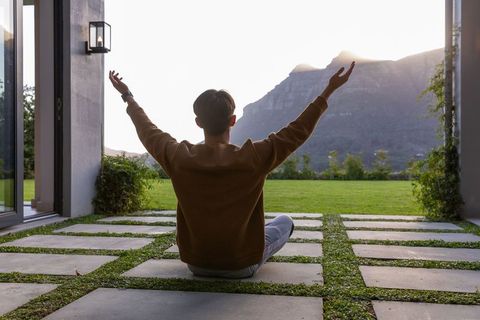 Man practicing meditation on modern paved patio with mountain sunset view