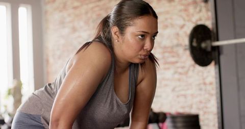 Determined female athlete pausing mid-workout in brick gym sweating after strength training