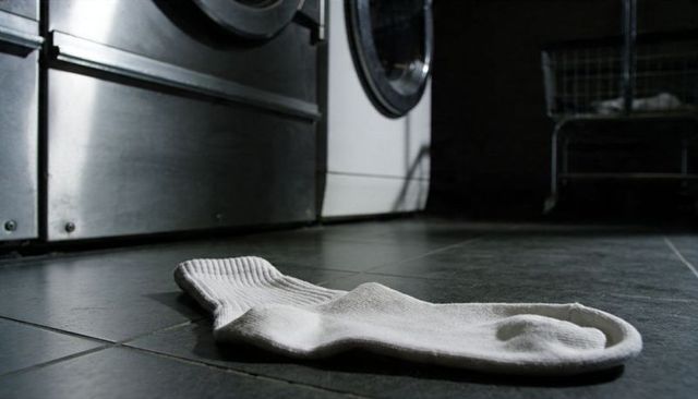 Single white crew sock lying on dark tiled laundromat floor near industrial washer and cart