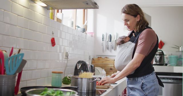 Image of caucasian mother with newborn baby in baby carrier cooking in kitchen. motherhood, parental love and taking care of newborn baby concept digitally generated image.