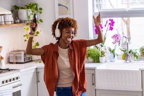 African american woman dancing and singing in bright modern kitchen wearing headphones