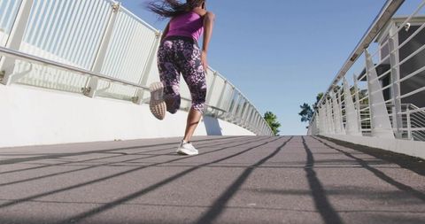 Female athlete sprinting up modern footbridge in purple tank and floral leggings