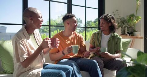 African american friends sipping coffee and laughing on sunlit sofa by large window