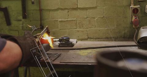Gloved welder using oxy-fuel torch melting steel on workbench, sparks flying, industrial workshop