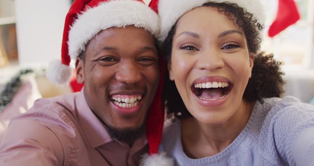 Happy couple wearing Santa hats, celebrating Christmas. They are smiling and cheerful, embracing holiday spirit indoors. Ideal for use in holiday greeting cards, festive ads, or social media posts promoting holiday joy and togetherness.