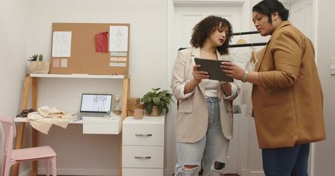 Diverse fashion designers collaborating over tablet and fabric swatches in compact studio
