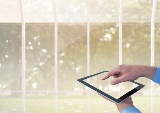 Digital composite of Hand touching tablet against trees and  windows