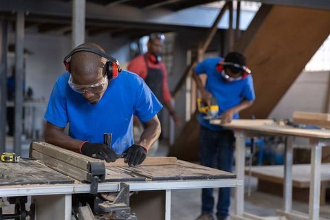 African american woodworkers cutting and trimming lumber in industrial workshop