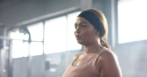 Determined woman training in gym with strong backlight, wearing headband and tank