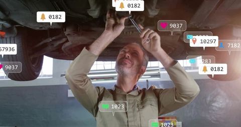 Mechanic tightening bolts under lifted car with wrench and augmented reality notifications