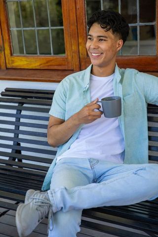 Relaxed Young Man with Mug Smiling on Porch Bench Outdoors
