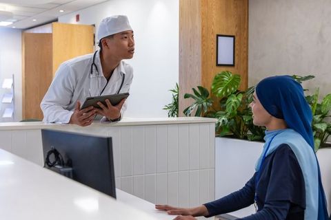Doctor consulting receptionist at modern clinic reception using tablet, collaborative care