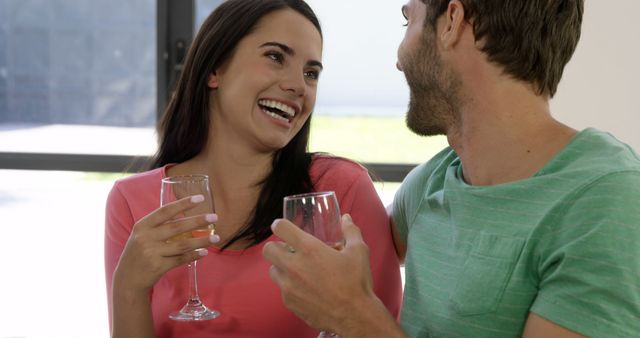 Happy couple enjoying each other's company while drinking wine indoors. Great for use in articles, blogs, and advertisements that discuss relationships, leisure time, relaxation, and social gatherings at home.