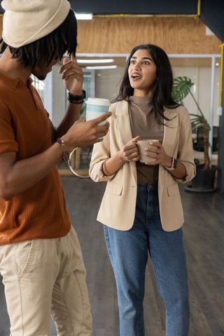 Colleagues chatting over coffee in modern office lounge, casual workplace conversation