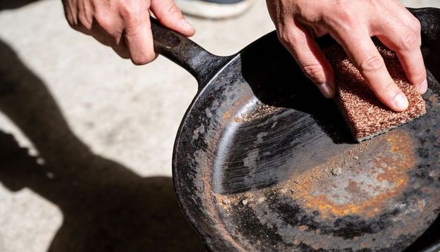 Restoring rusted cast iron skillet scrubbing with abrasive scouring pad hands close-up