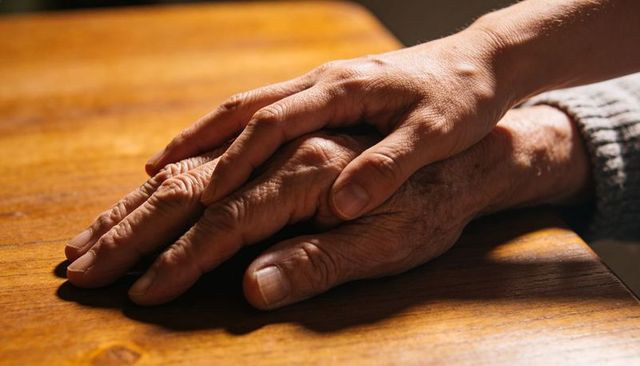 Holding senior hand offering gentle support and compassion on warm wooden surface