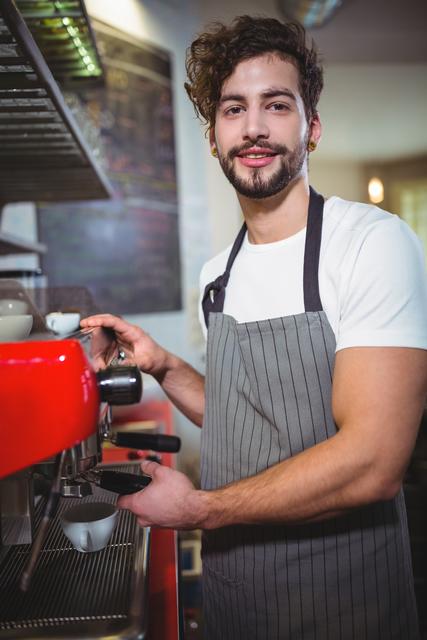 Portrait of waiter making cup of coffee at counter in kitchen at cafÃ©