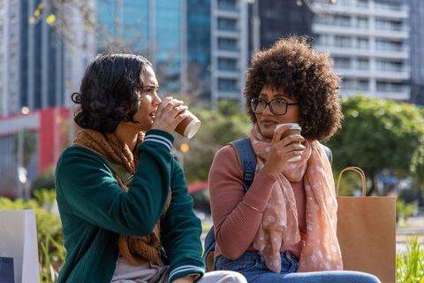 Multiracial friends sipping coffee and chatting on urban bench, casual downtown lifestyle
