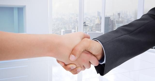 This digital composite shows a close-up of a handshake between two businesspeople in a modern office with a city skyline in the background. Ideal for use in articles, presentations, promotional materials, and business-themed websites to represent partnerships, successful agreements, and professional relationships.