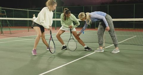 Female tennis players stretching at net during group training session on outdoor courts