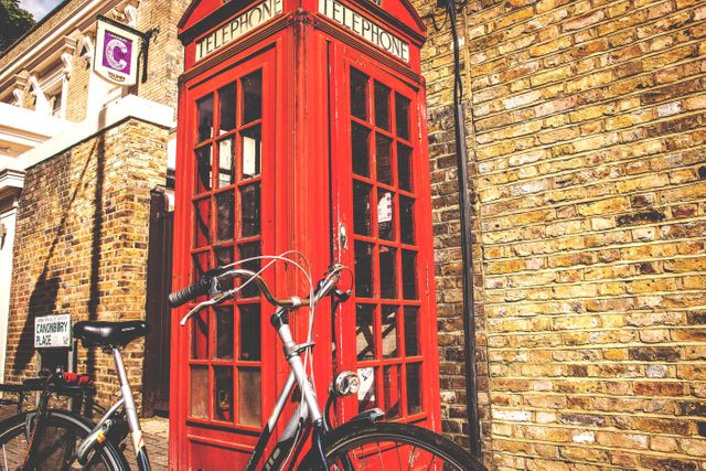 Depicting the quintessential British red telephone box with a bicycle leaning against it, this scene brings out the charm and character of London streets. The brick wall adds a touch of vintage urban life, suitable for use in travel promotions, cultural articles, or lifestyle blogs highlighting British landmarks and city life.