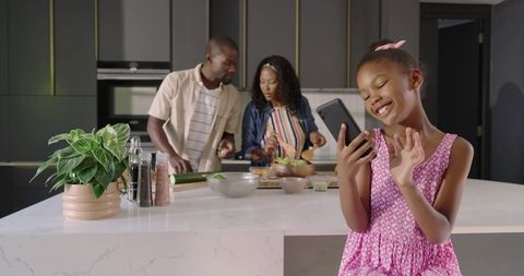 African American family cooking together while daughter video calling on smartphone