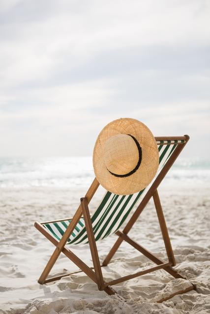 Straw hat kept on empty beach chair at tropical sand beach