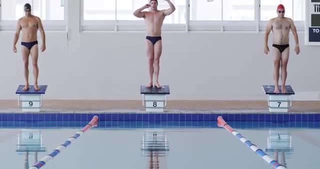 This dynamic image captures a group of male swimmers preparing to dive off starting blocks during a swimming competition. Ideal for illustrating swimming events, athletic performance, sports training, and competitive spirit.