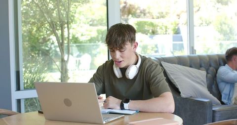 Teen Studying at Laptop with Headphones and Smartwatch in Sunny Living Room